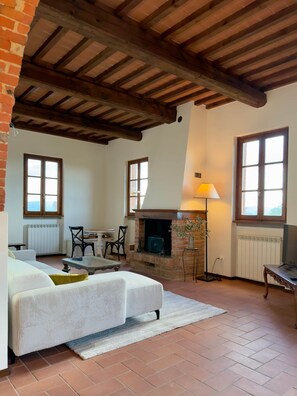 Ein gemütliches Wohnzimmer mit Kamin, einer Couch, einem Esstisch und zwei Fenstern.
