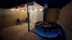 Ein überdachter Außenbereich mit Whirlpool, Sitzgelegenheiten und einer Tür mit blauen Paneelen.