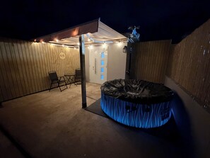 A covered outdoor area with a hot tub, seating, and a door with blue panels. - Description (Fajardo)
