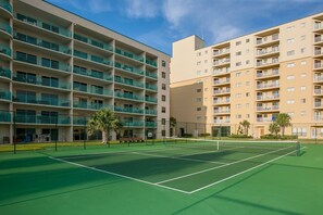 A tennis court with a net, surrounded by multi-story buildings with balconies. - Gulf Shores Plantation Palms 6603 | Pool + Hot Tub (Gulf Shores)