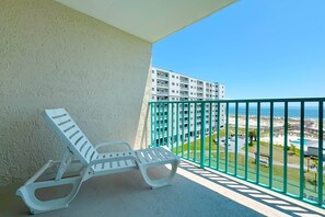 Ein Balkon mit einer weißen Liege, Blick auf einen Strand und einem Hochhaus im Hintergrund.