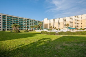 A hotel with multiple floors, a well-maintained lawn, and a white fence. - Gulf Shores Plantation Palms 6603 | Pool + Hot Tub (Gulf Shores)