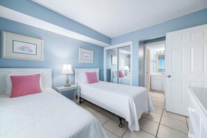 A hotel room with two beds, a nightstand with a lamp, and a door leading to a bathroom. - Gulf Shores Plantation Palms 6603 | Pool + Hot Tub (Gulf Shores)