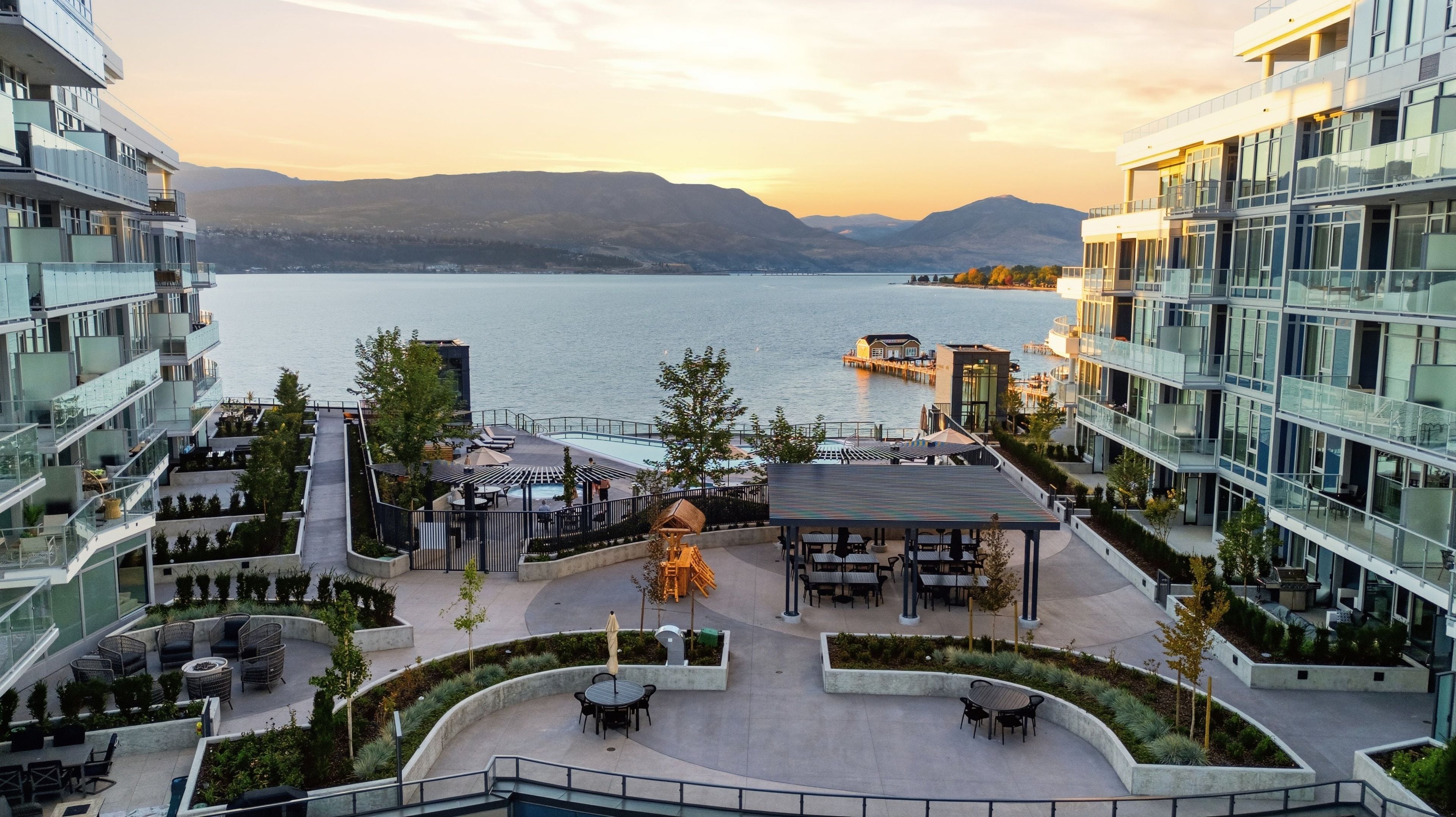 A modern hotel with a rooftop terrace overlooking a lake, featuring outdoor seating and a view of the mountains.