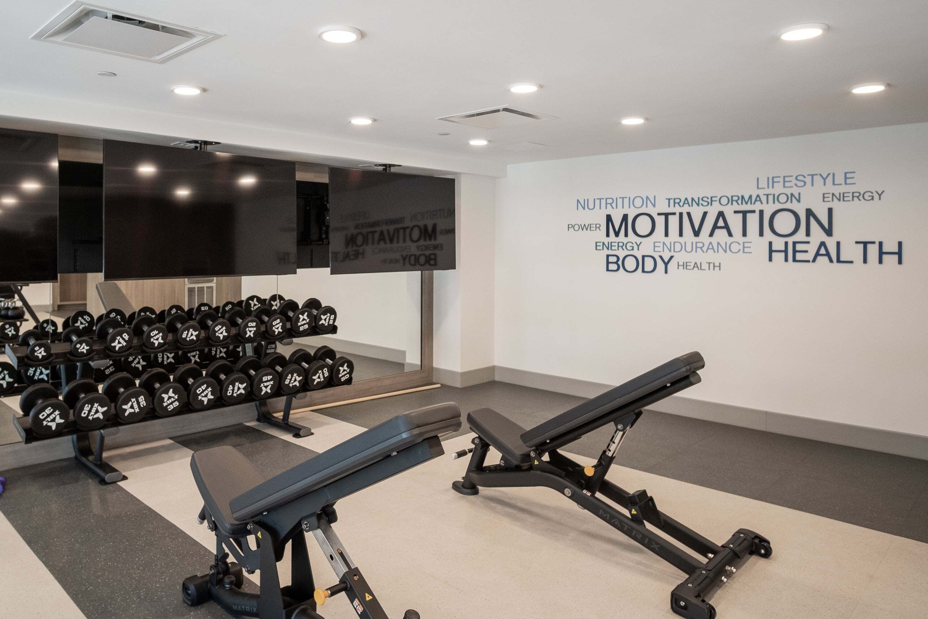 Ein Fitnessstudio mit Krafttrainingsgeräten, Kurzhanteln und einer Wand mit motivierenden Sprüchen.