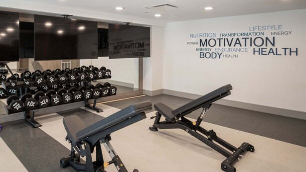 Ein Fitnessstudio mit Krafttrainingsgeräten, Kurzhanteln und einer Wand mit motivierenden Sprüchen.