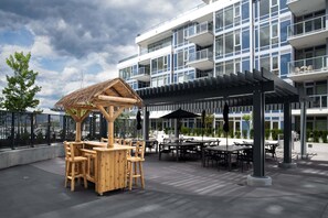 A modern building with a covered outdoor seating area and a wooden play structure. - The Aqua Collection - Lakeview Terrace - 902 (Kelowna)