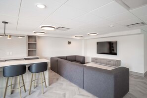 A modern kitchen with a built-in island, bar stools, and a flat-screen TV mounted on the wall. - The Aqua Collection - Lakeview Terrace - 902 (Kelowna)