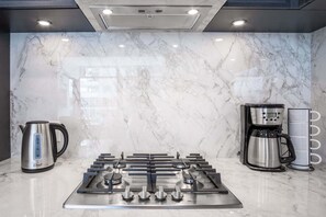 A modern kitchen with a gas stove, a coffee maker, and a kettle. - The Aqua Collection - Lakeview Terrace - 902 (Kelowna)