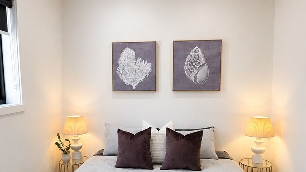 Een net opgemaakt bed met een groene plaid, twee ingelijste kunstwerken aan de muur en bedlampjes.
