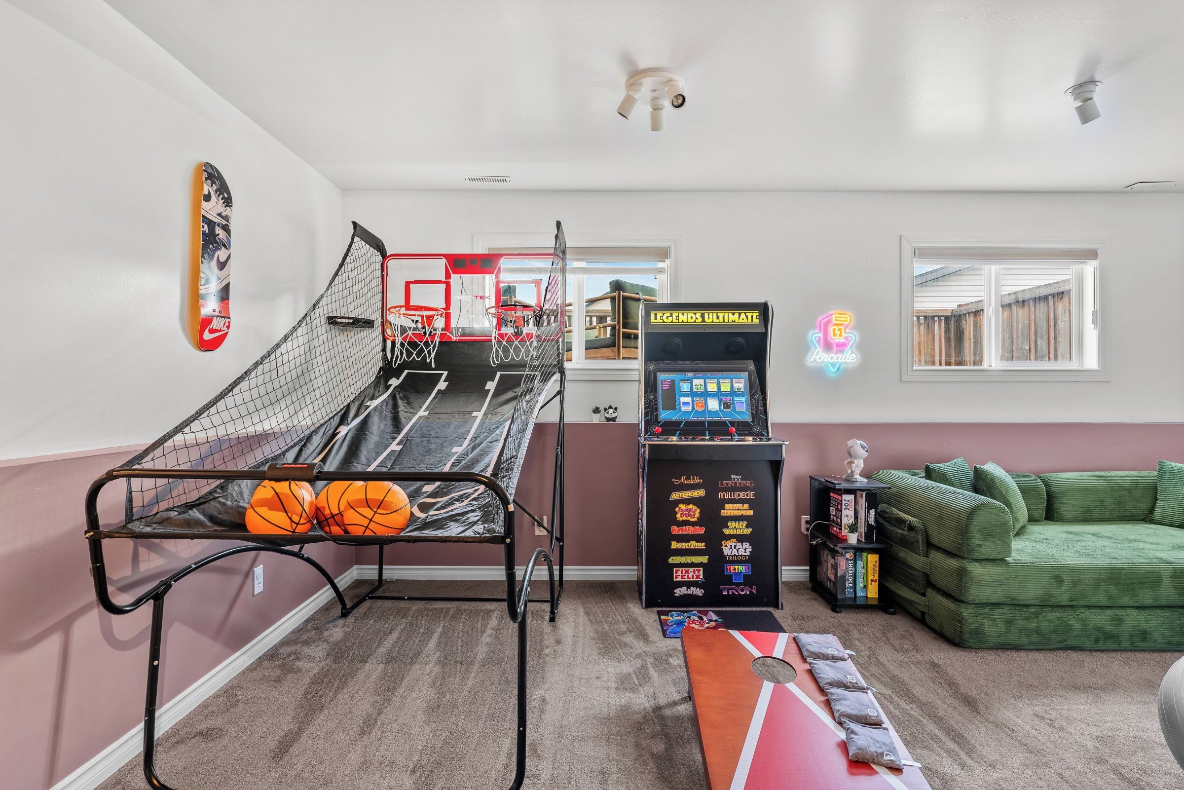 A room with a basketball hoop, a gaming console, a green couch, and a window with a view.