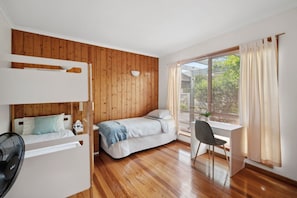 Quarto com beliche, escrivaninha e cadeira, paredes de madeira e janela com persianas.