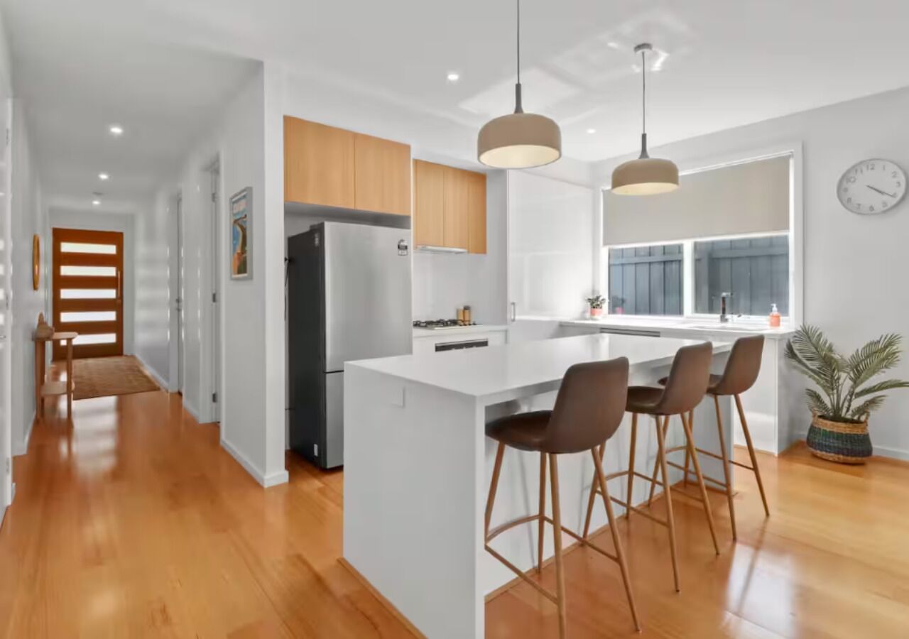 A modern kitchen with white cabinetry, a central island with bar stools, and pendant lighting.