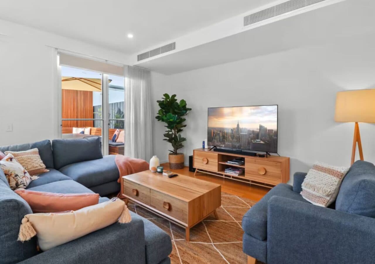 A modern living room with a sofa set, a coffee table, a TV, and a plant.