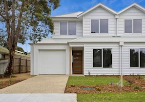A two-story house with a garage, a front door, and a small front yard with a tree and a fence. - Driftwood – Luxury Coastal Townhouse in the Heart of Ocean Grove (Ocean Grove)