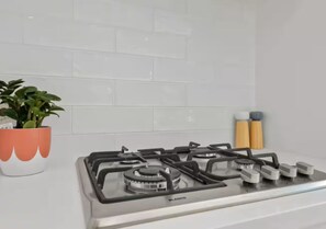 A kitchen with a gas stove, a potted plant, and two containers on the counter. - Driftwood – Luxury Coastal Townhouse in the Heart of Ocean Grove (Ocean Grove)