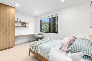 Ein Schlafzimmer mit einem Bett, einem Sessel, einem Kleiderschrank, einem Fenster und einem Regal mit Dekoration.