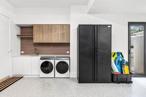Eine moderne Küche mit Waschmaschine, einem schwarzen Kühlschrank und einem Stauraum voller Taschen.