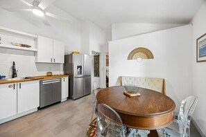 Eine moderne Küche mit weißen Schränken, Edelstahlgeräten und einem Essbereich mit Holztisch und klaren Stühlen.