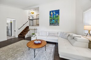 Ein modernes Wohnzimmer mit einem weißen Sofa, einem Holztisch und einem Bild an der Wand.