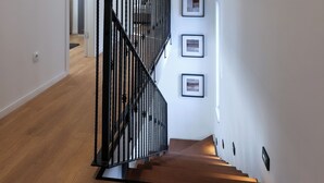 Un interior moderno con una escalera de madera, paredes blancas y cuadros enmarcados.