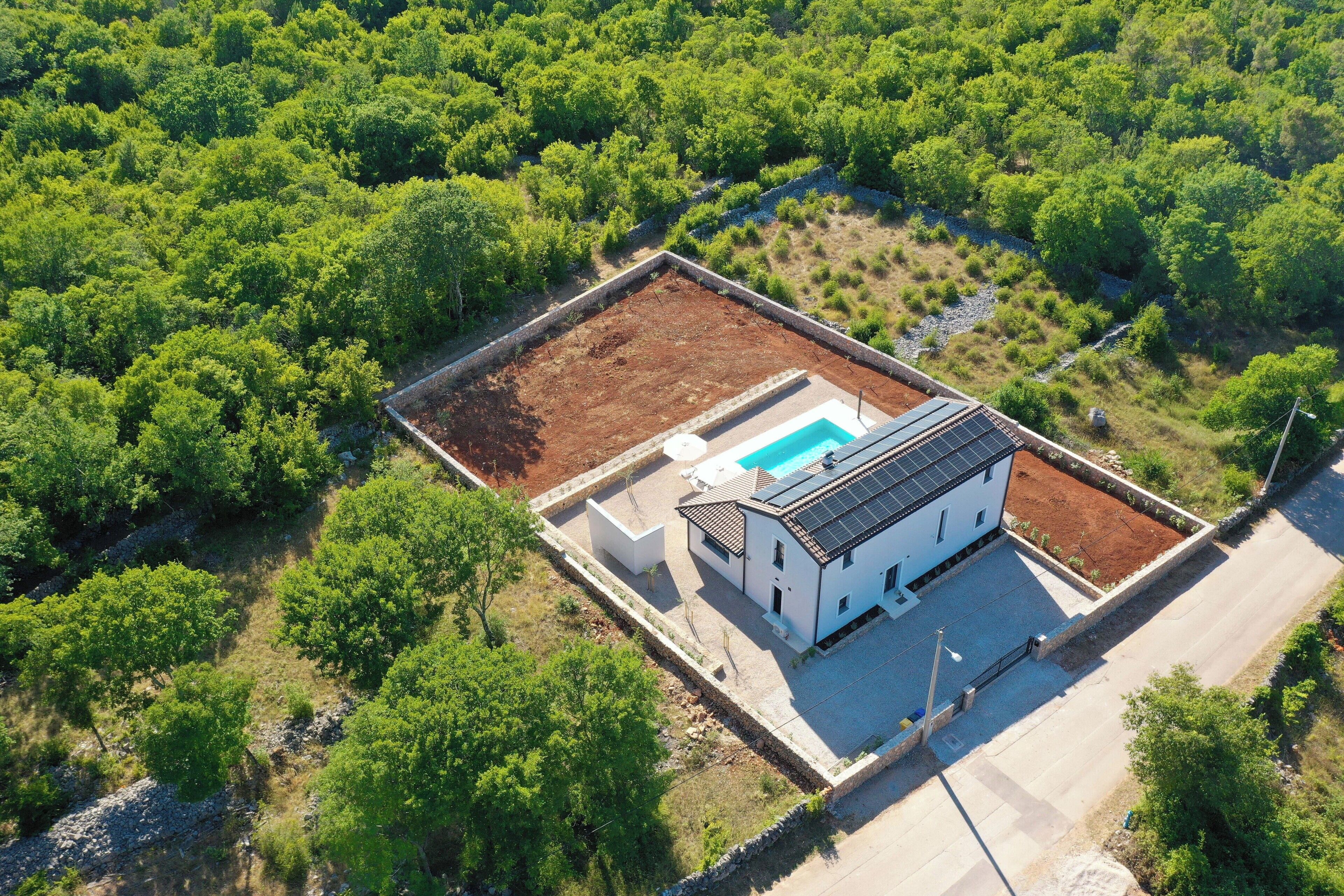 Vue aérienne d’une maison moderne dotée d’une piscine, entourée d’une végétation luxuriante.