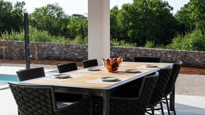 Un espacio de comedor al aire libre con una mesa y sillas, un frutero y un muro de piedra al fondo.