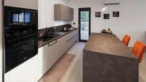 Una cocina moderna con microondas, horno y estufa integrados, un comedor con una mesa grande y sillas naranjas, y una puerta que da a un balcón.