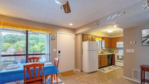 A compact kitchen with wooden cabinets, a refrigerator, and a dining area with a table and chairs. - Starfish Haven|Lake View|Pool| Boat Ramp| Sleeps6 (Lake Ozark)