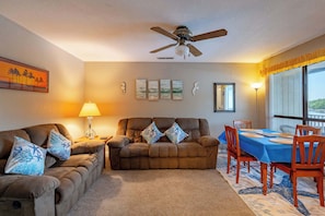 A living room with a ceiling fan, a dining table with chairs, a sofa set, and wall art. - Starfish Haven|Lake View|Pool| Boat Ramp| Sleeps6 (Lake Ozark)