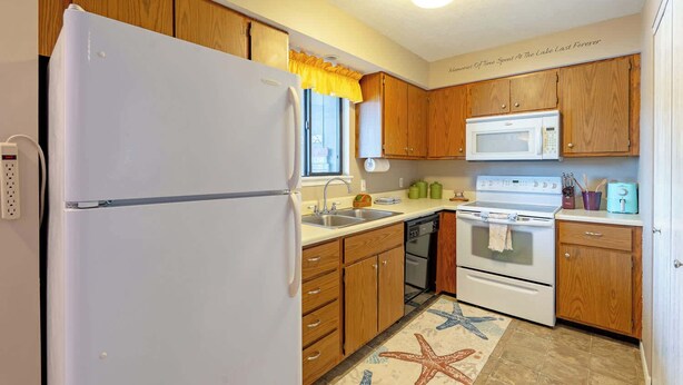 A kitchen with wooden cabinets, a white refrigerator, a microwave, an oven, and a sink. - Starfish Haven|Lake View|Pool| Boat Ramp| Sleeps6 (Lake Ozark)