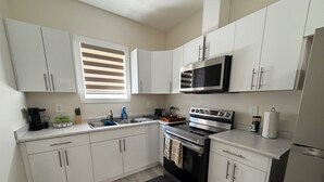 A modern kitchen with white cabinets, stainless steel appliances, a black countertop, and a window with blinds. - Superb and spacious 2-bedroom apartment in peaceful Saskatoon neighborhood (Saskatoon)