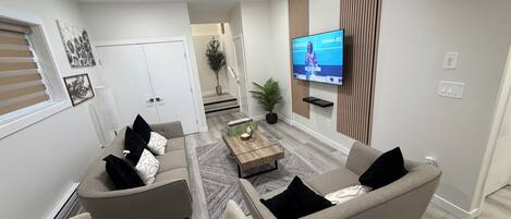A modern living room with a sofa, armchairs, a coffee table, and a flat-screen TV mounted on the wall.