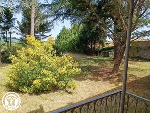 A garden with a metal fence, trees, and a stone wall. - Gîtes de France® - Domaine de Hauterive (VIRE SUR LOT)