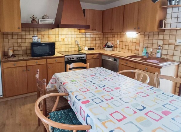A compact kitchen with wooden cabinets, a microwave, a stove, and a sink. - Gîtes de France® - Domaine de Hauterive (VIRE SUR LOT)