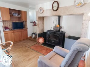 A living room with a sofa, a television, a fireplace, and a kitchen area with wooden cabinets. - Gîtes de France® - Domaine de Hauterive (VIRE SUR LOT)
