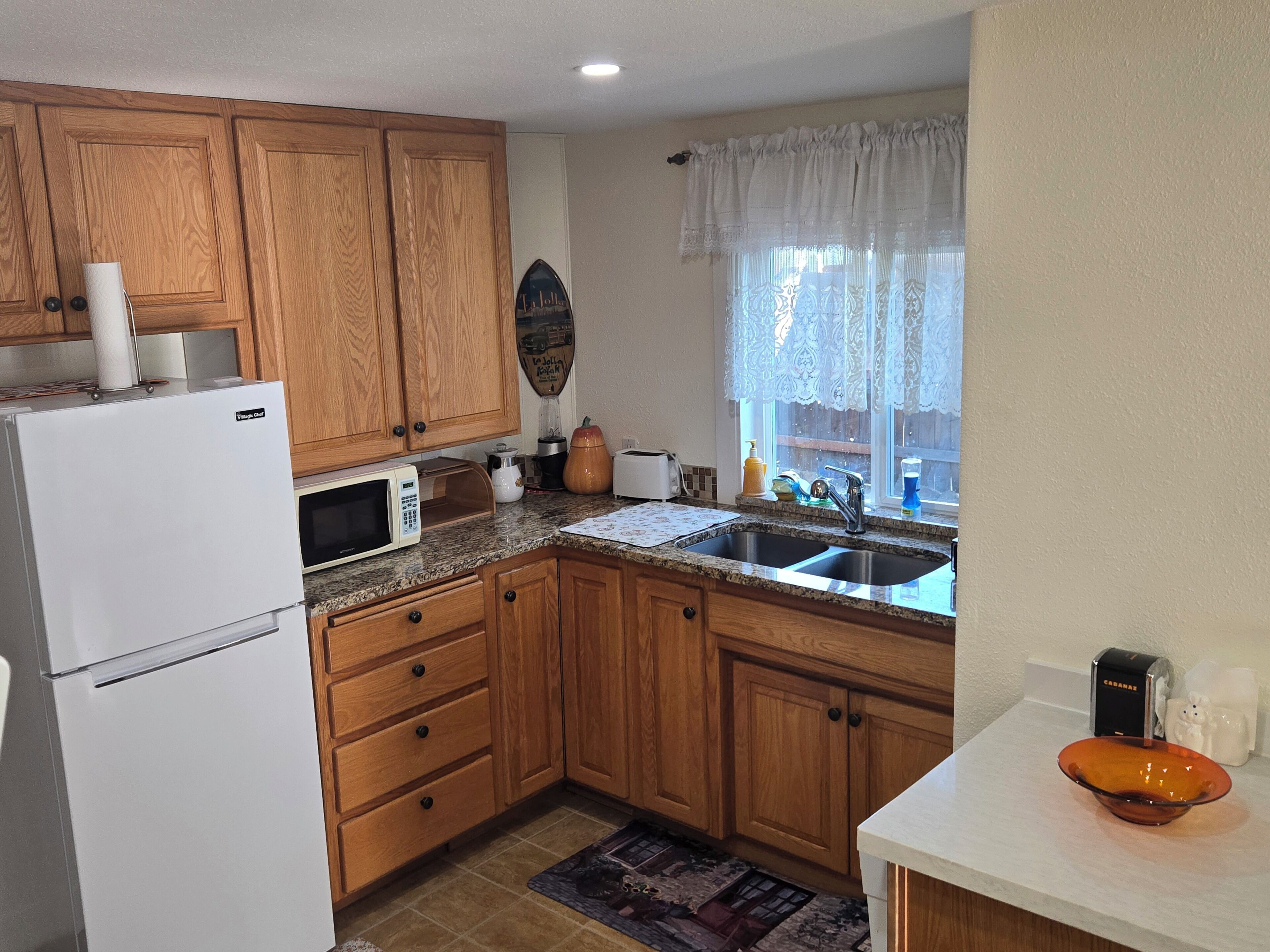 A kitchen with wooden cabinets, a refrigerator, a microwave, a sink, and a window with a view.