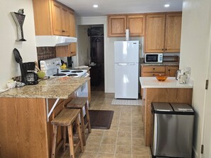 A kitchen with wooden cabinets, a white refrigerator, a microwave, a stove, and a sink.