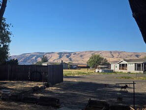 Un paysage rural caractérisé par un ciel dégagé, une clôture en bois, un portail en métal et un bâtiment doté d’un porche.