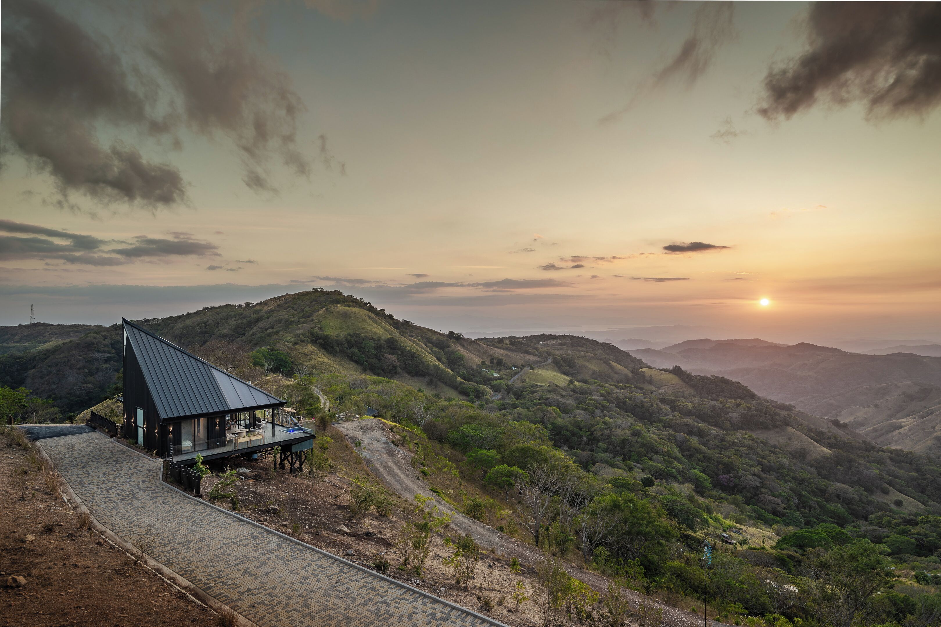 A house with a sloped roof, a paved driveway, and a view of rolling hills.