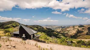 Un edificio moderno con techo inclinado, rodeado de terreno montañoso y vegetación escasa.