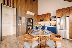 A modern kitchen with wooden cabinets, a stainless steel refrigerator, and a dining area with a round table and chairs.