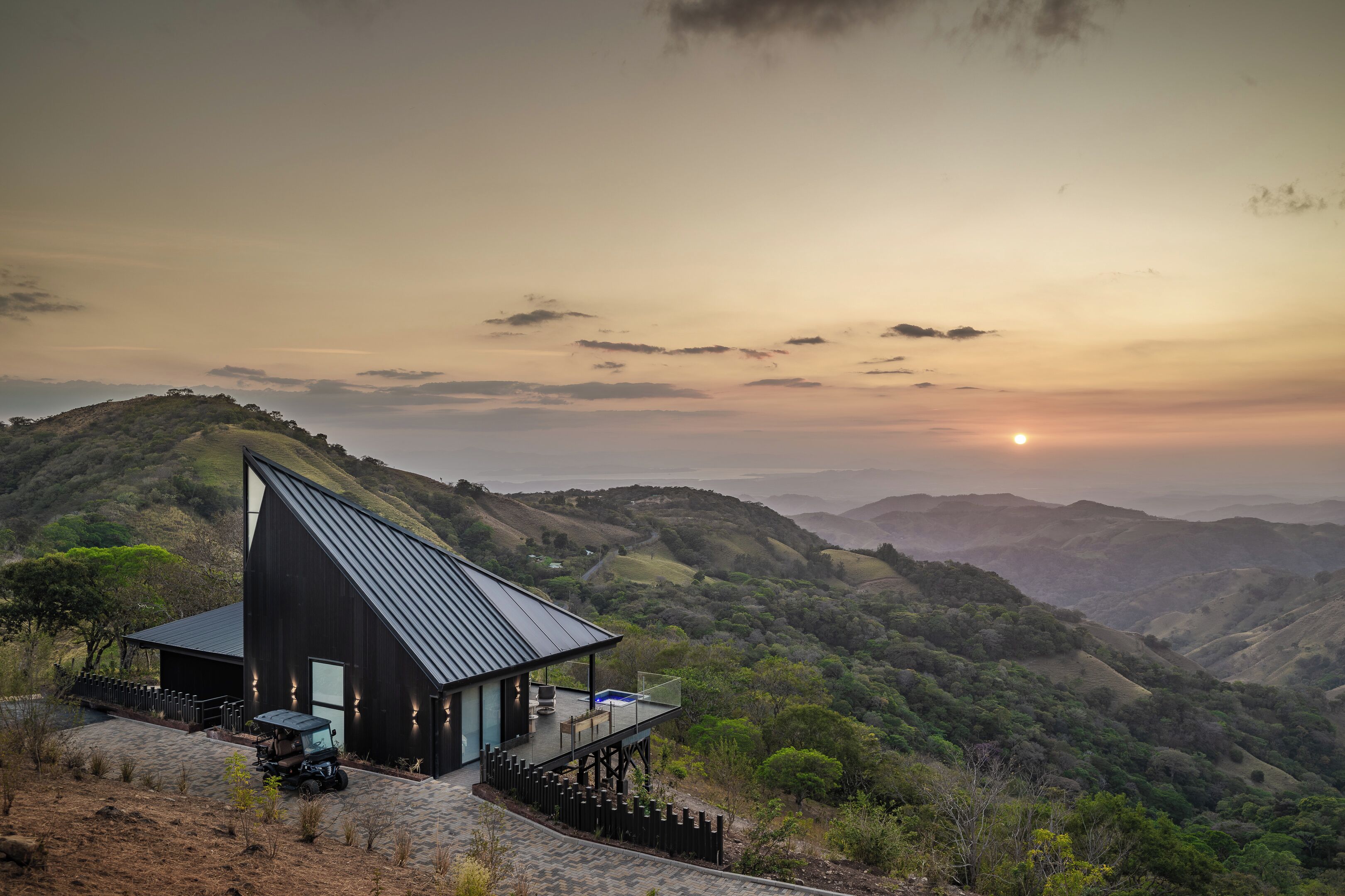 A modern house with a sloped roof, a deck, and a view of rolling hills.