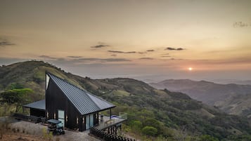 A modern house with a sloped roof, a deck, and a view of rolling hills.