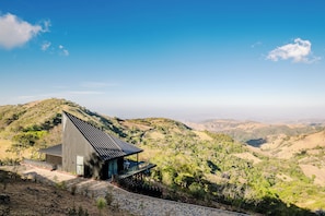 A modern building with a sloped roof, a covered outdoor seating area, and a view of a hilly landscape.