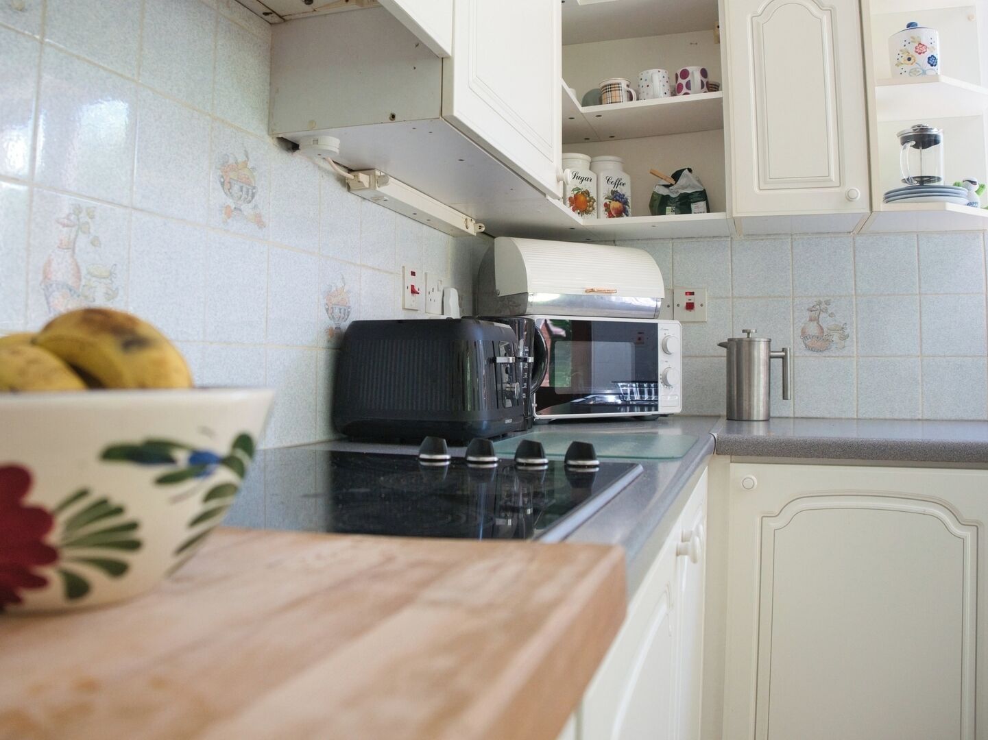 A kitchen with white cabinets, a microwave, a toaster, and a bowl of fruit on the counter.