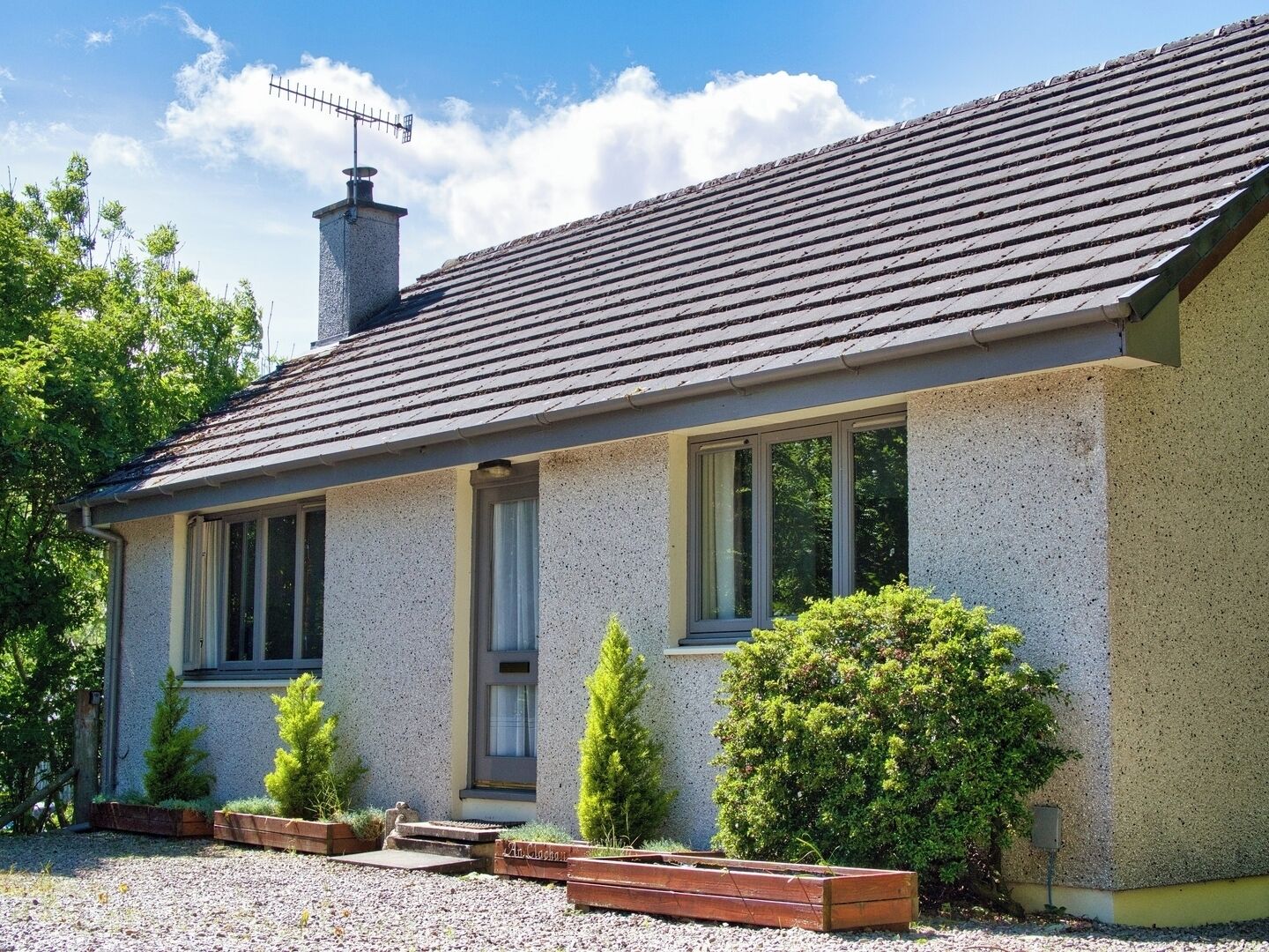 A single-story house with a sloped roof, a chimney, and a window with a curtain.