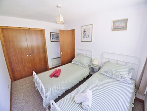 Ein Schlafzimmer mit zwei Einzelbetten, Holzschränken, einer Deckenleuchte und gerahmten Bildern an der Wand.