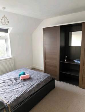 Um quarto com uma cama, um guarda-roupa, um radiador e uma janela.