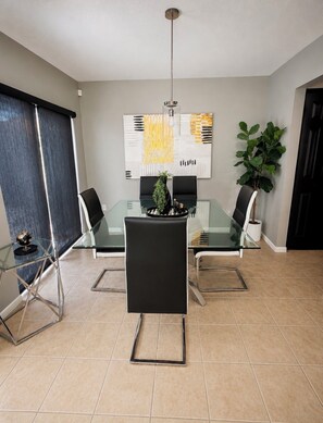 A modern dining area with a glass table, black chairs, a decorative plant, and a contemporary art piece on the wall.